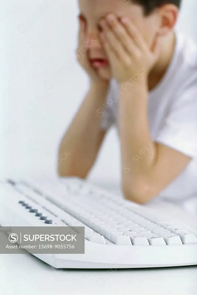 Boy holding head, computer keyboard in foreground
