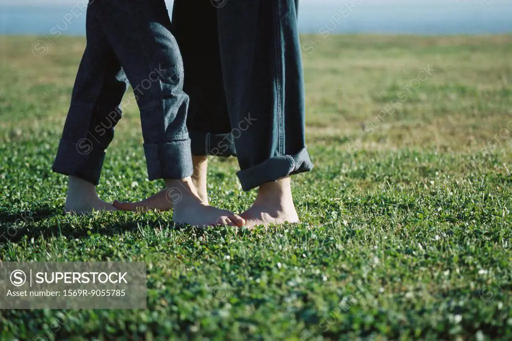Young couple standing barefoot in field, low section
