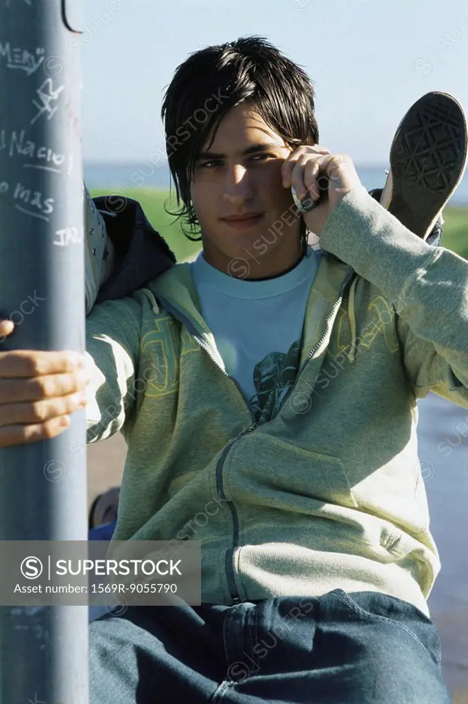Teenage boy using cell phone, friend´s feet resting on his shoulders