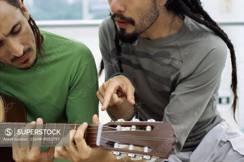 Man teaching friend to play acoustic guitar