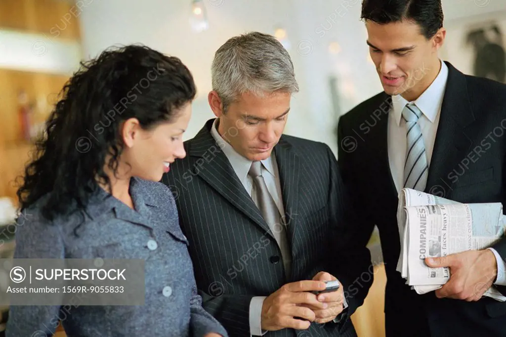 Business associates standing together, looking at cell phone