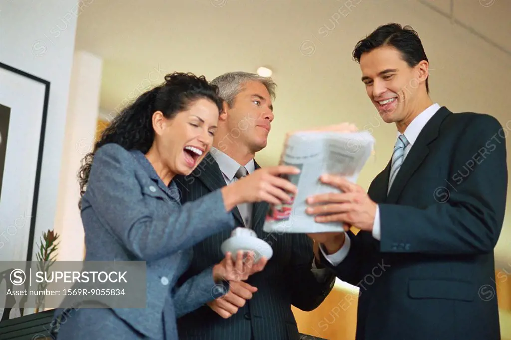 Group of executives looking at newspaper and laughing