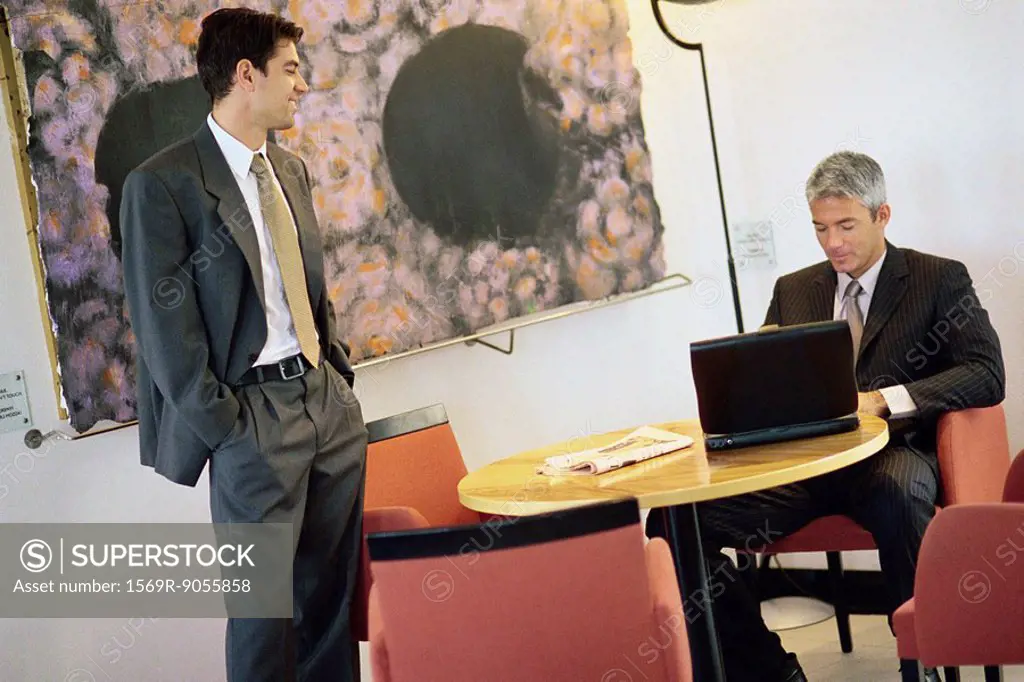 Businessmen chatting in break room, one using laptop computer