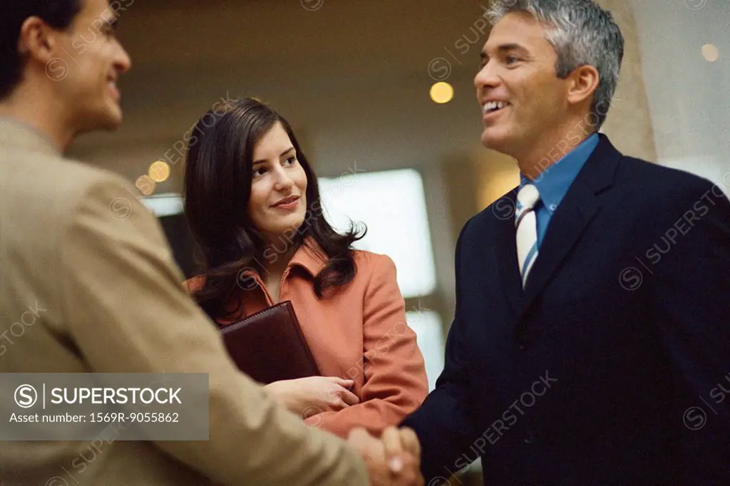 Businessmen shaking hands, female colleague standing nearby