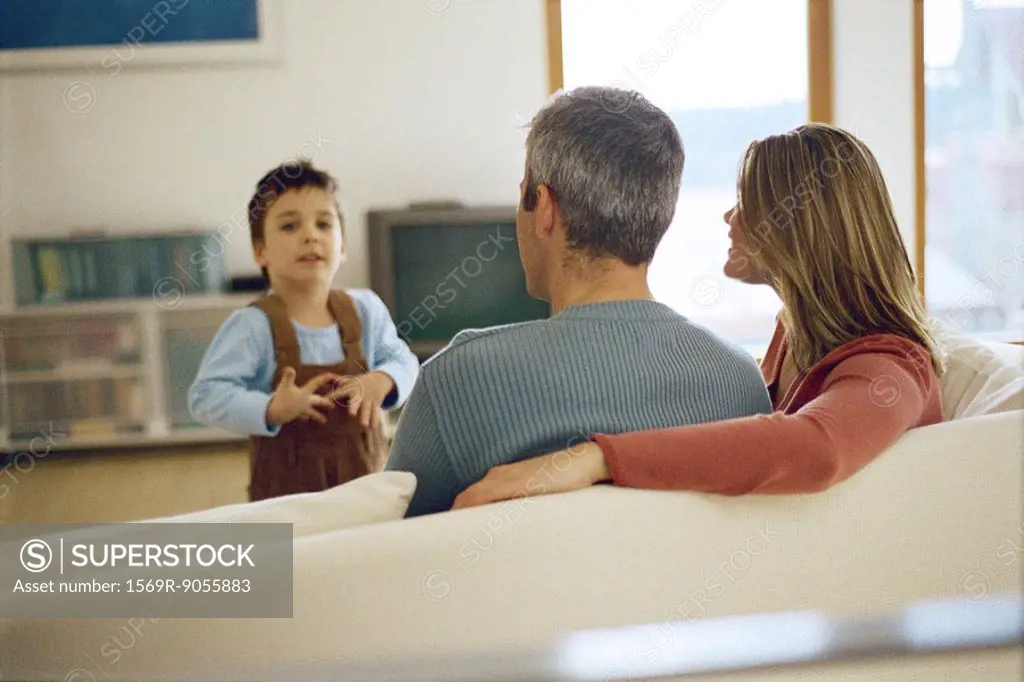 Little boy talking to his parents sitting on the sofa