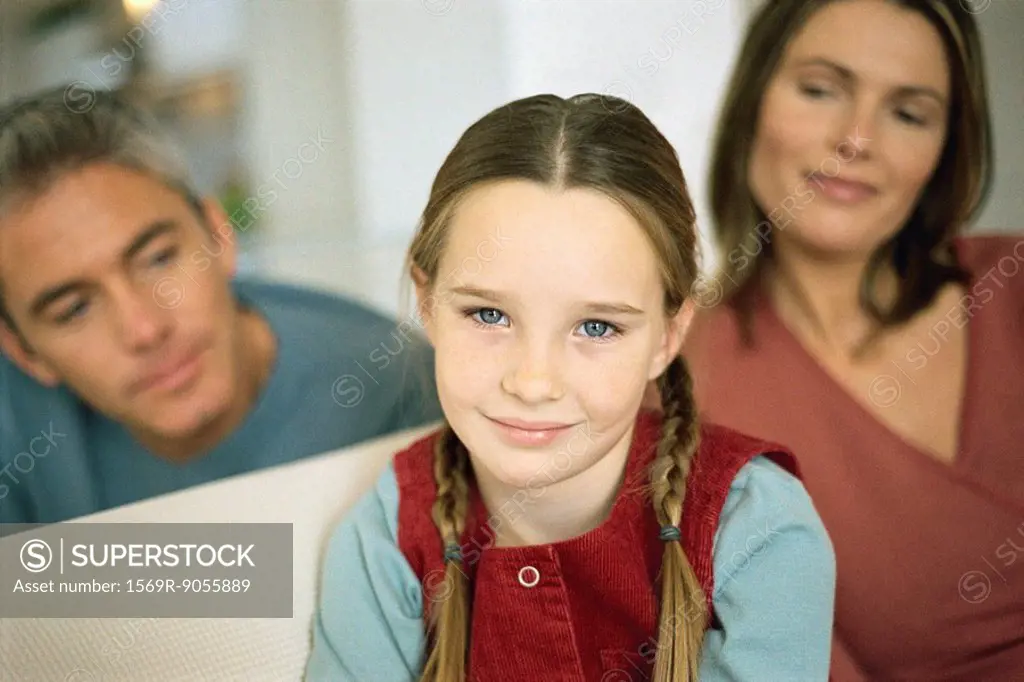 Little girl smiling at camera, parents in background