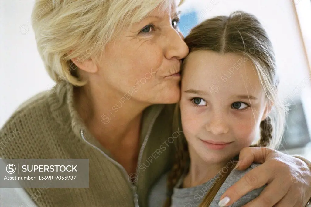 Senior woman with arm around granddaughter, kissing forehead, portrait