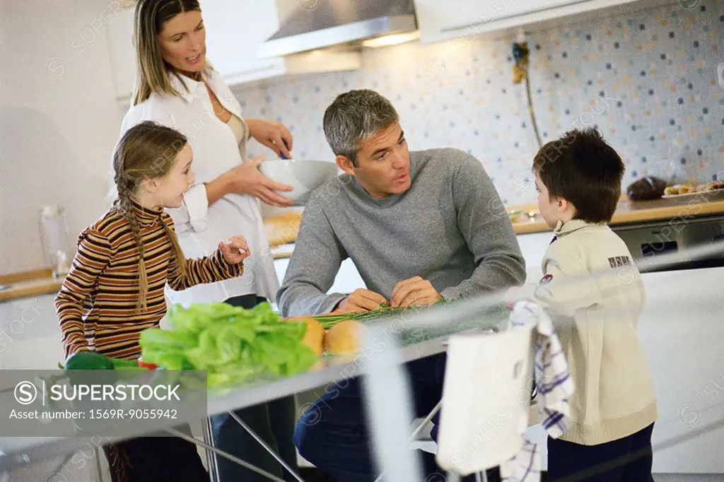 Family together in kitchen all listening to little boy