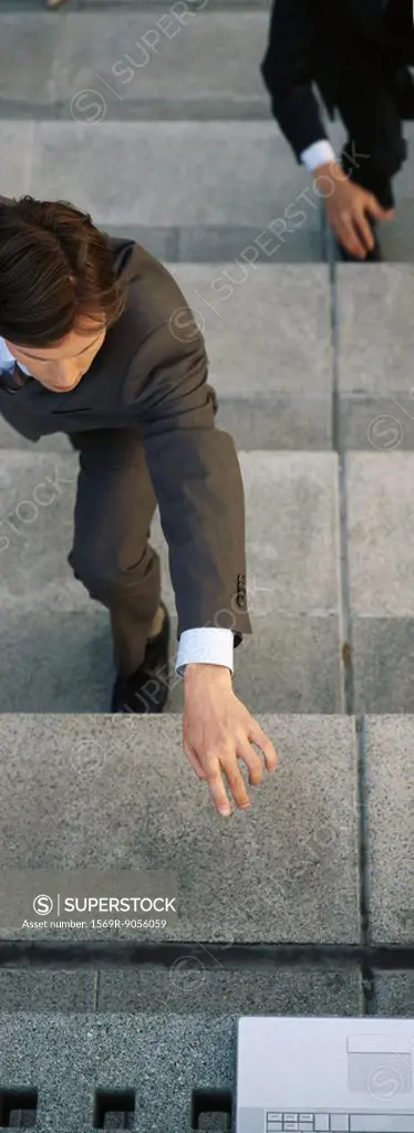 Businessmen crouching on steps reaching for laptop computer set at top of stairs