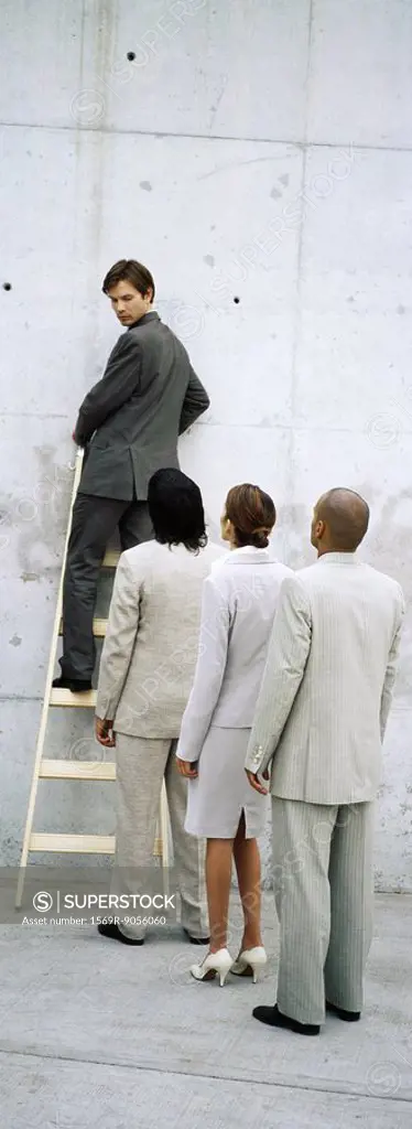 Businessman climbing ladder, looking over shoulder at professionals lined up behind him