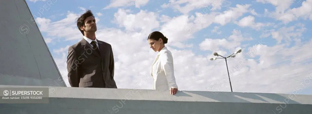 Businessman and businesswoman standing on rooftop, man looking at view, woman looking down