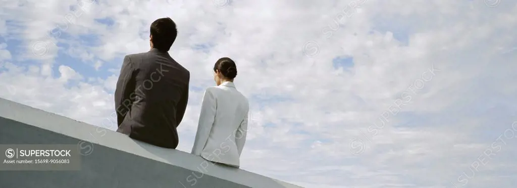 Businessman and businesswoman sitting side by side on rooftop ledge