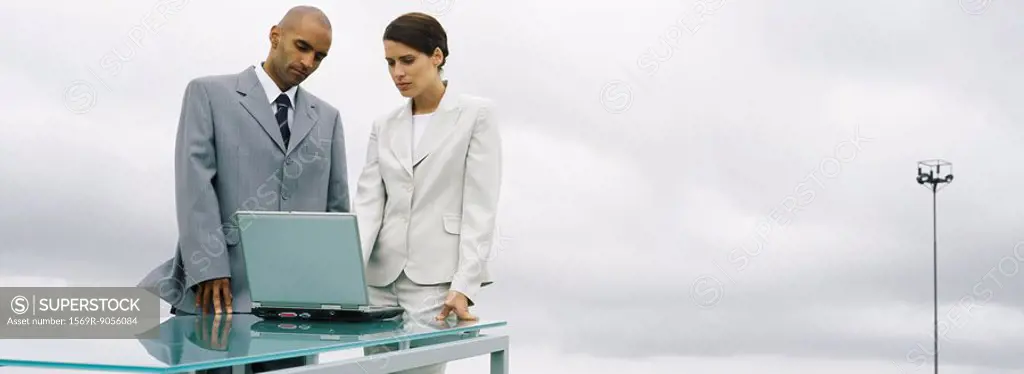 Business associates standing together outdoors, looking at laptop computer
