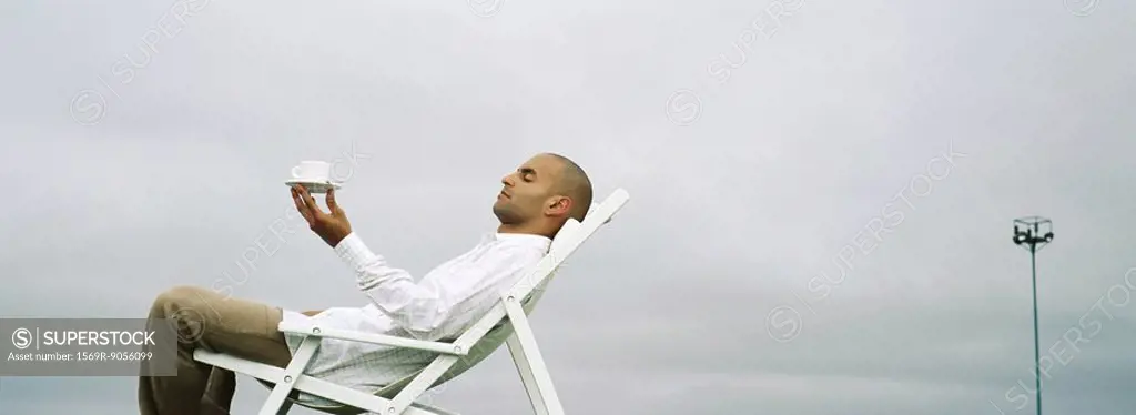 Man relaxing in deckchair, holding up coffee cup