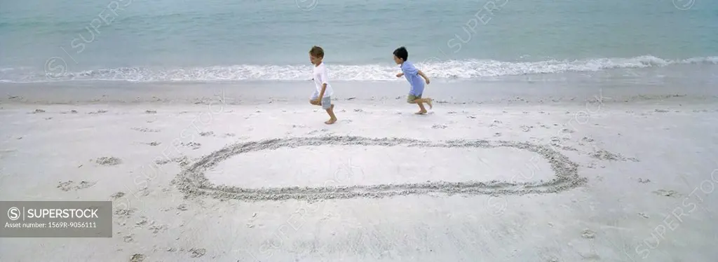 Boys running on beach, chasing each other around circle drawn in sand