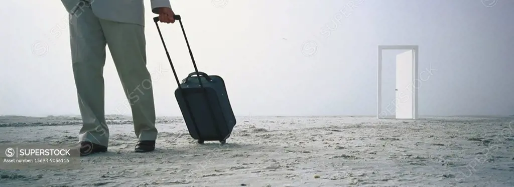Man walking with rolling luggage on beach, open door in distance