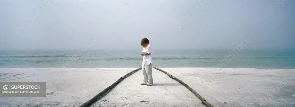Little boy sulking on beach, arms folded