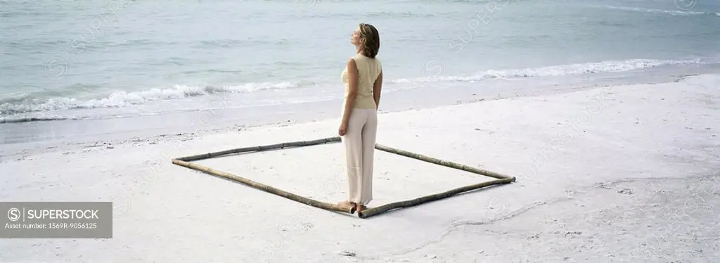 Woman standing in corner of square outlined on beach by lengths of bamboo