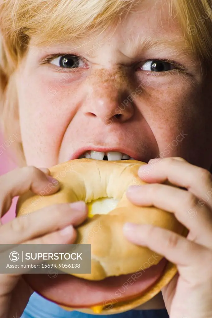 Boy biting into ham and cheese bagel sandwich, close_up