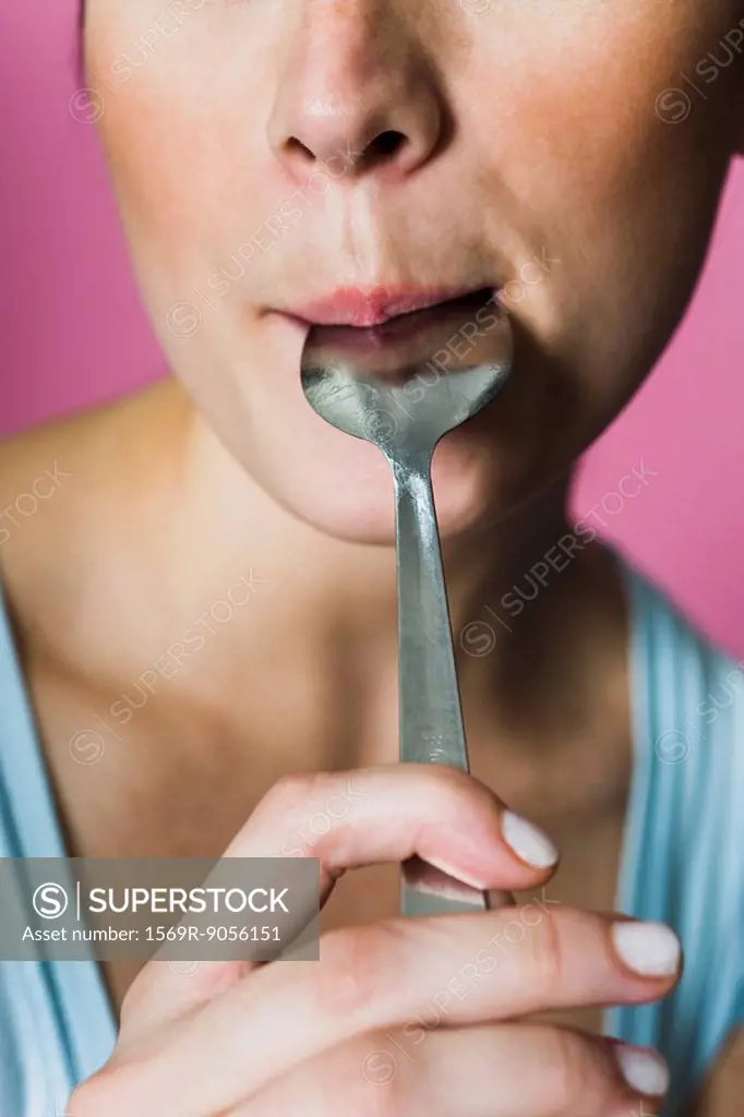 Woman licking spoon, cropped