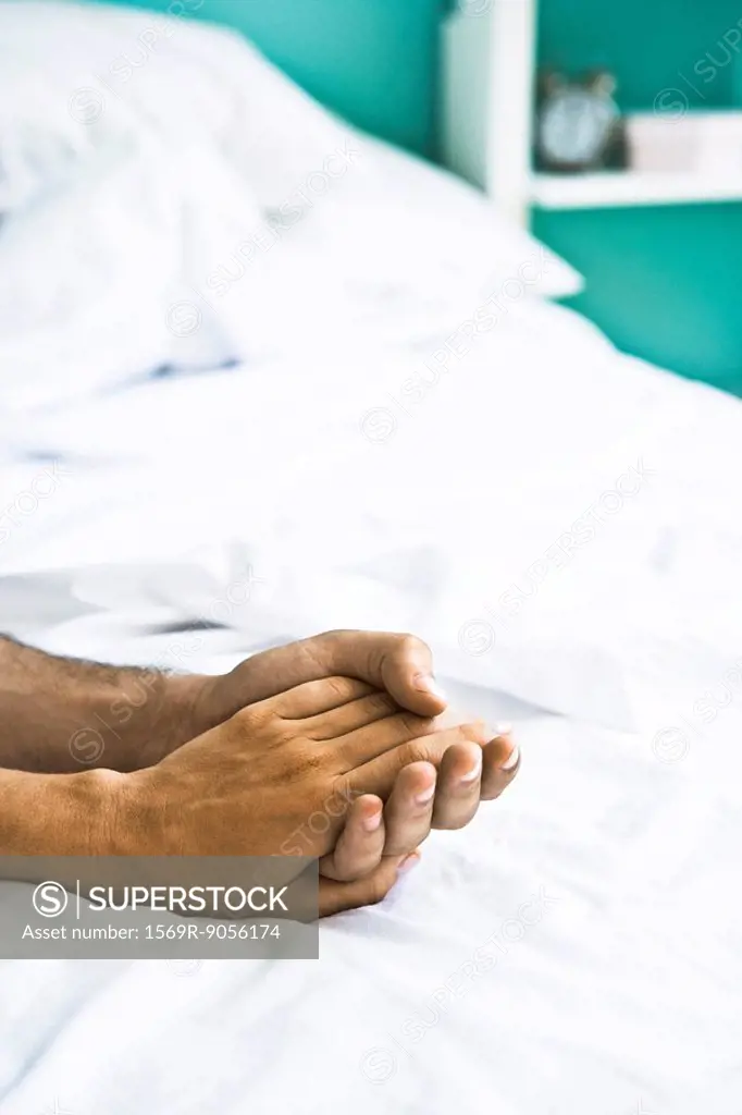 Couple´s clasped hands on bed