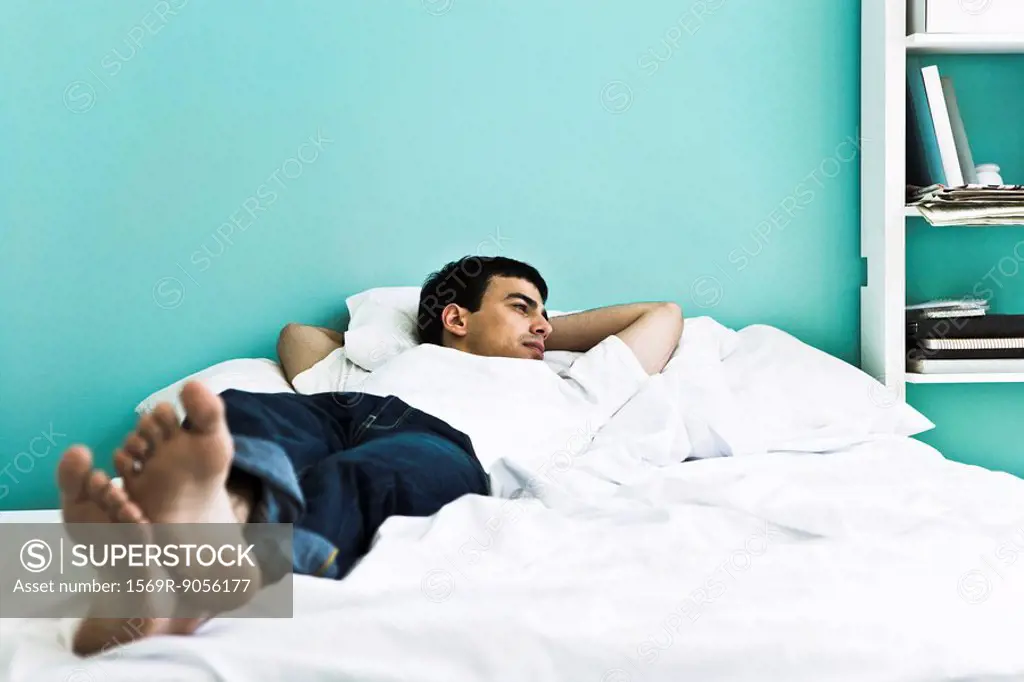 Man reclining on bed with arms behind head