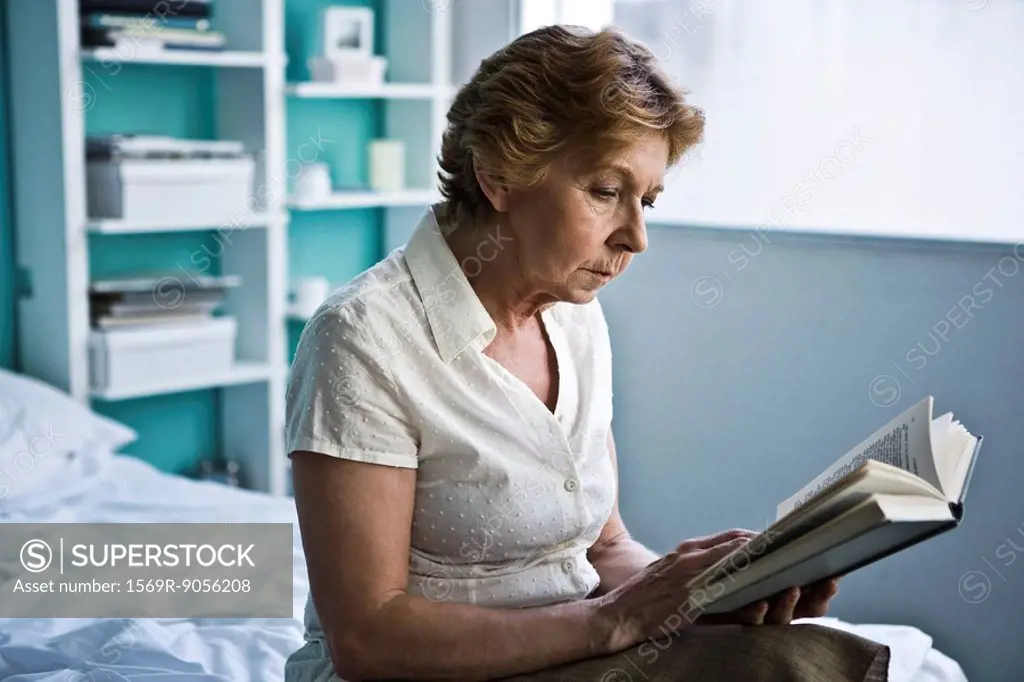 Senior woman sitting on bed reading book