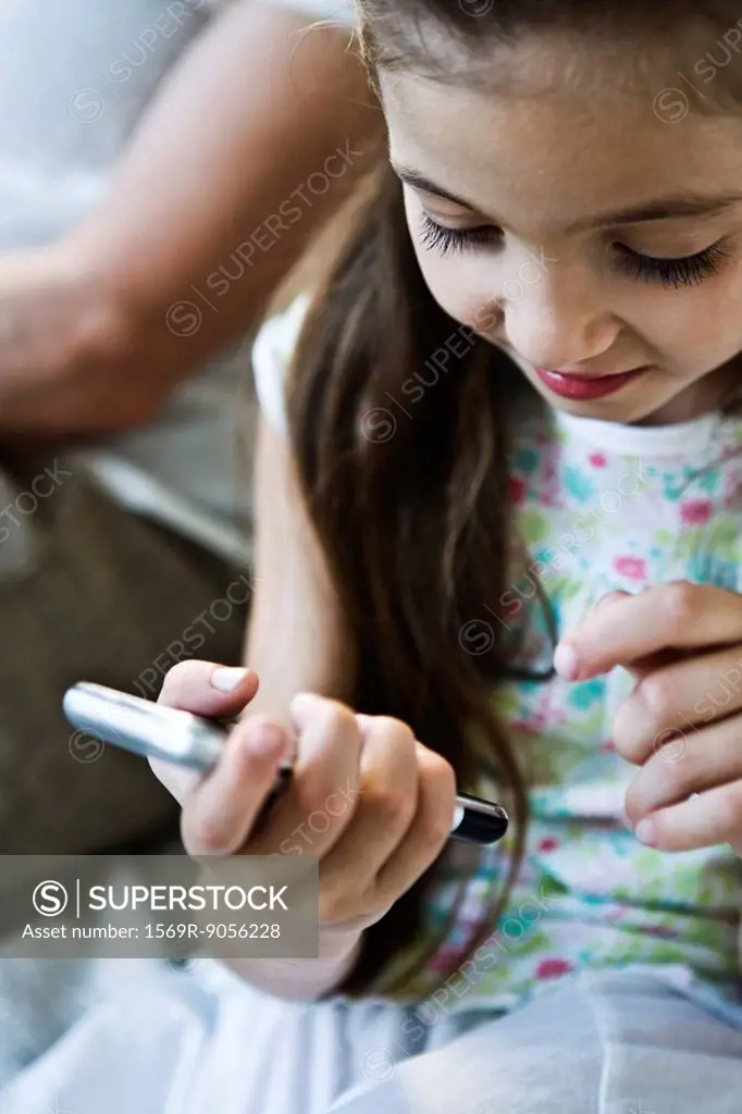 Little girl looking at cell phone, woman in background