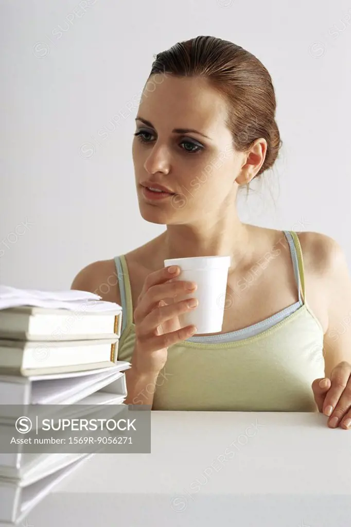 Woman on break looking with curiosity at stack of books and binders