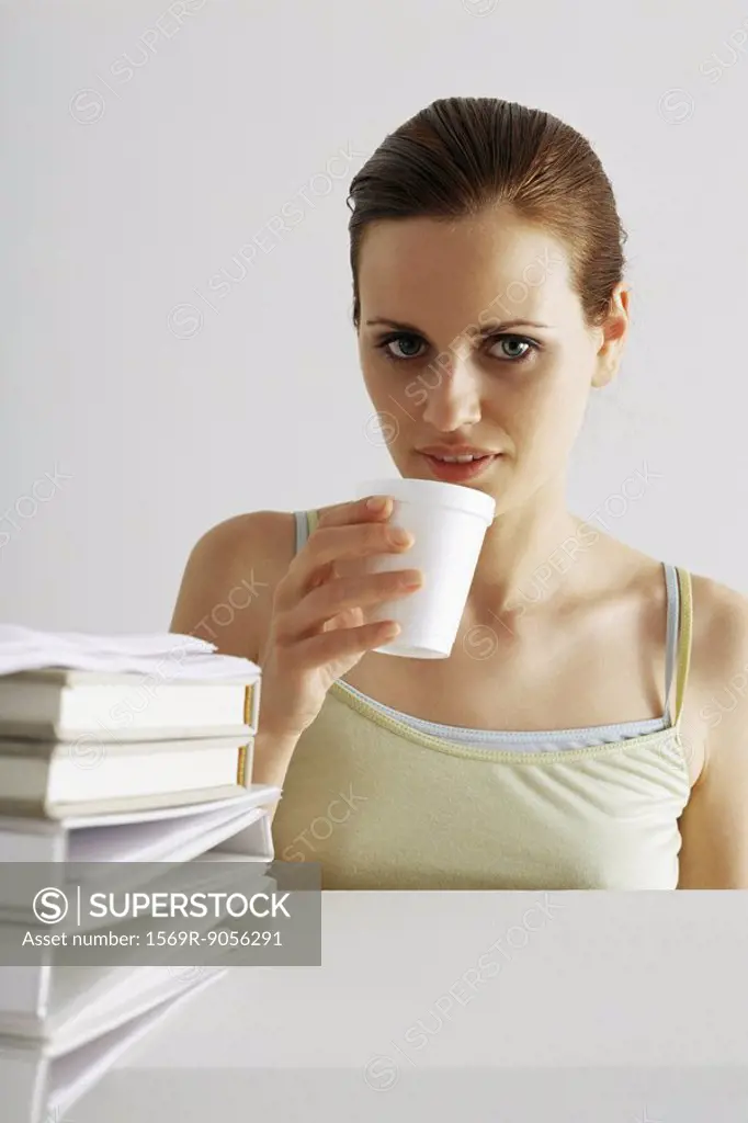 Woman taking break, drinking from disposable cup, stack of binders in foreground