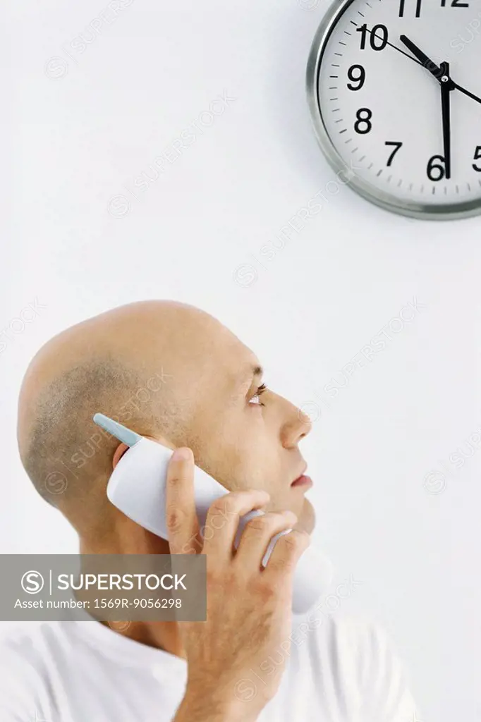 Man on phone call, looking over shoulder at clock