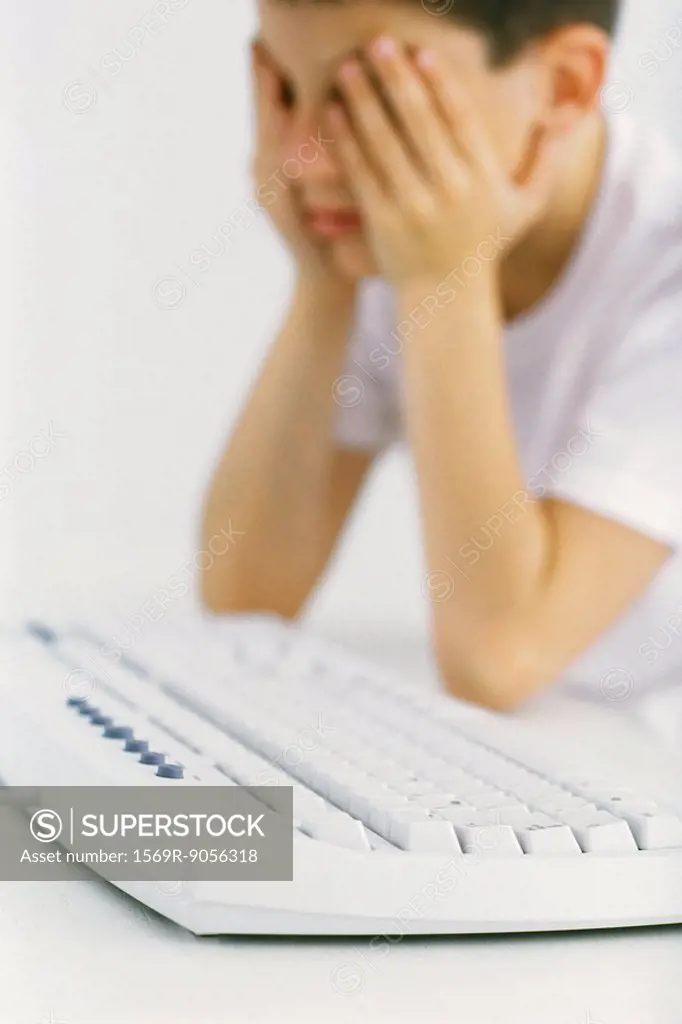 Boy at computer keyboard holding head