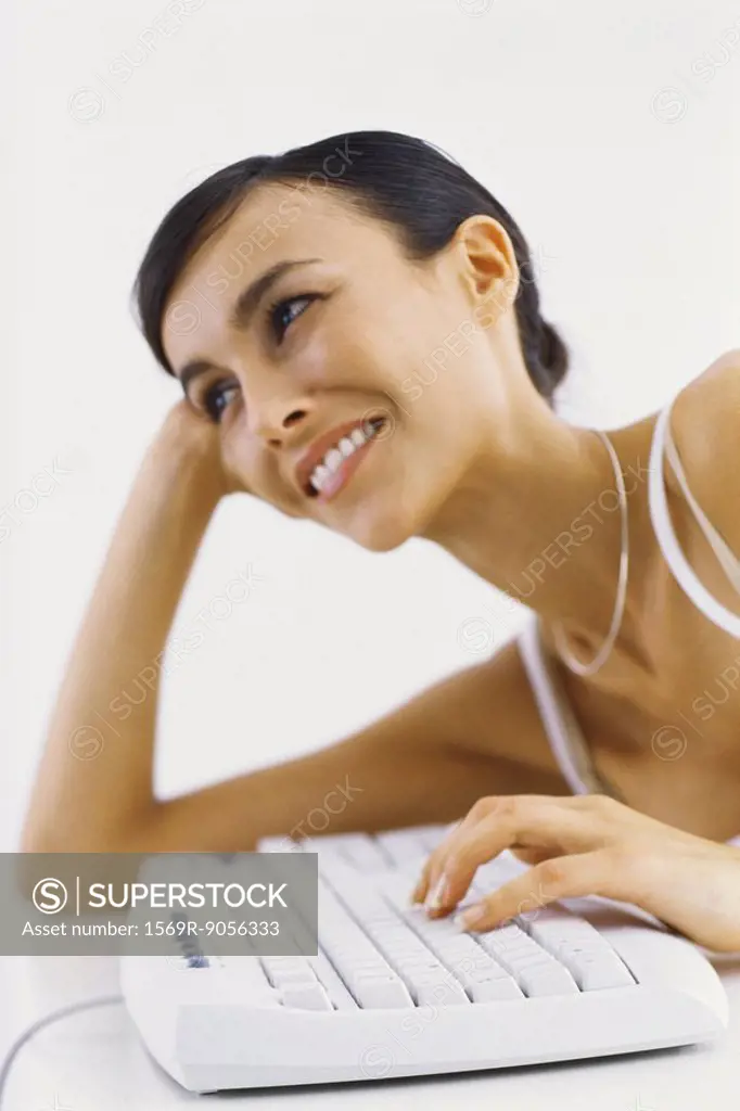 Woman leaning on elbow typing on keyboard, smiling
