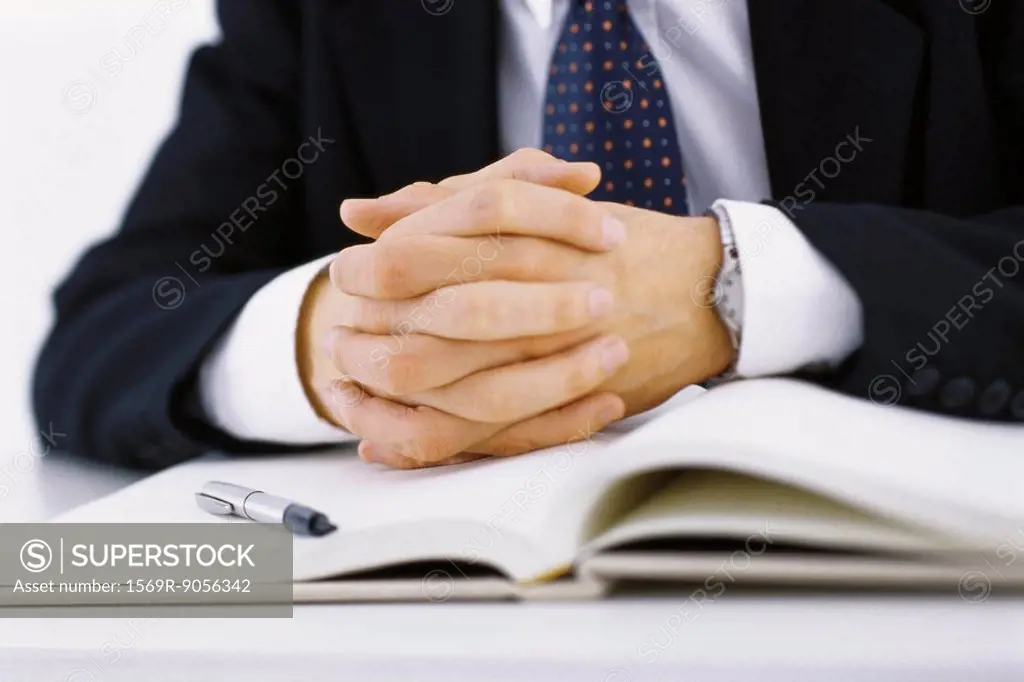 Businessman with hands clasped resting on open book, cropped