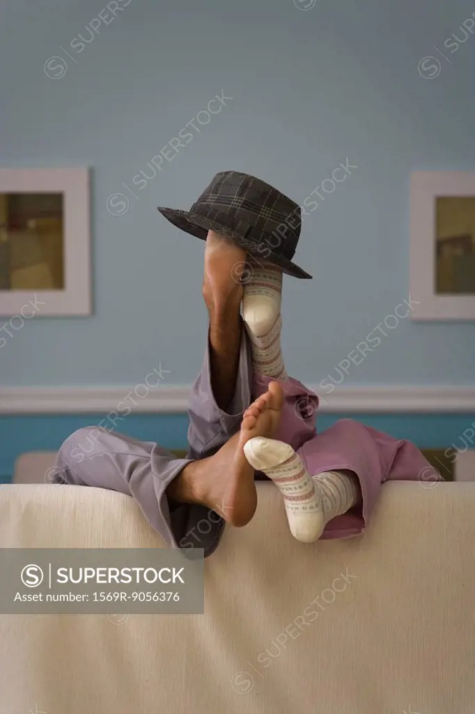 Two people reclining on sofa, legs raised together, hat set atop feet, rear view