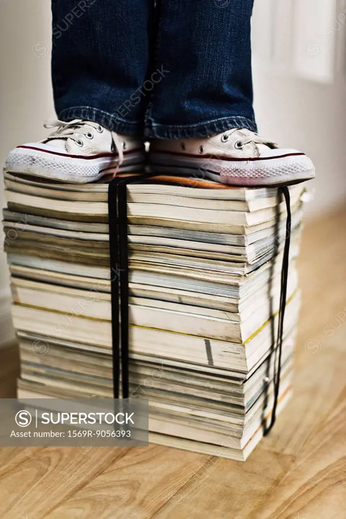 Person standing on top of bound stack of books and magazines