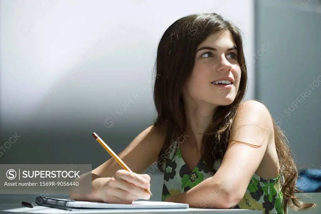 Teenage girl writing in notebook, dreamily looking away