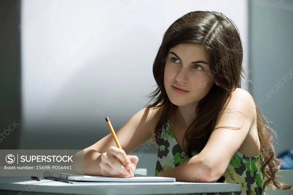 Teenage girl writing in notebook, contemplatively looking away