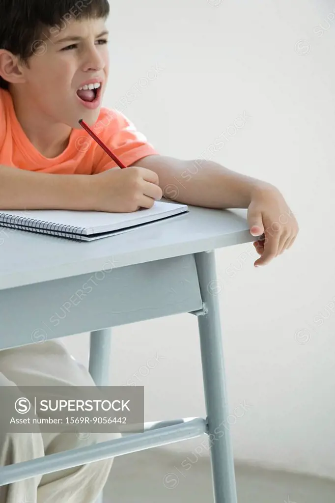 Elementary school student taking notes in classroom, squinting at board