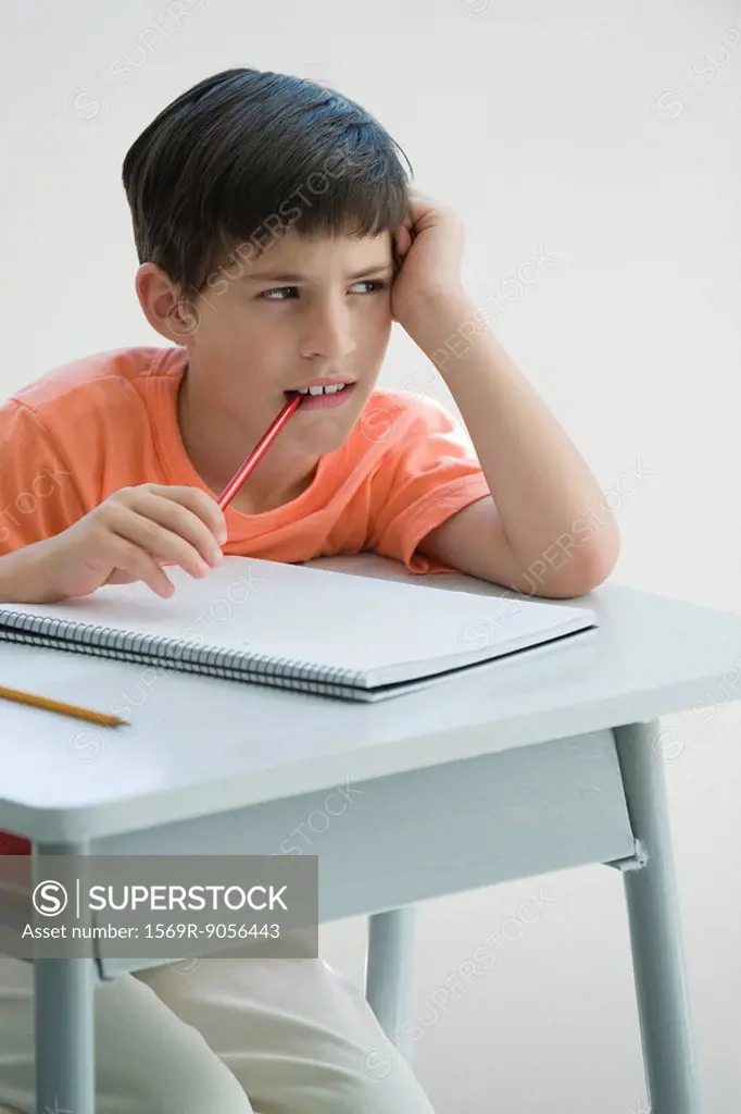 Elementary school student sitting at desk, leaning on elbow, chewing end of pencil