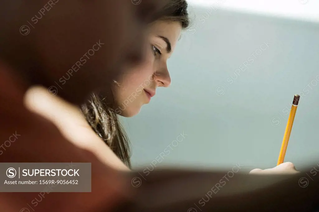 Teenage girl writing in class, side view