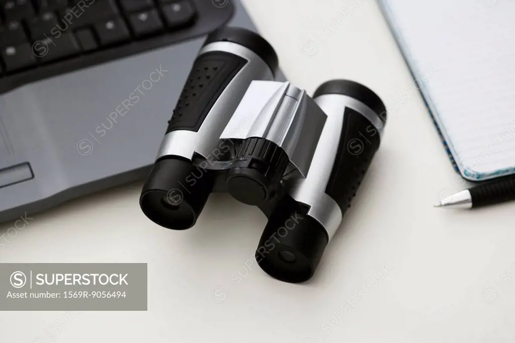 Binoculars on desk with laptop computer and notebook
