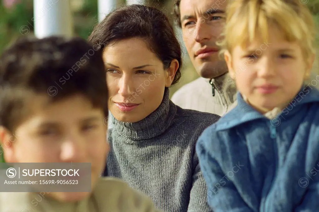 Woman sitting outdoors with husband and children, looking away in thought