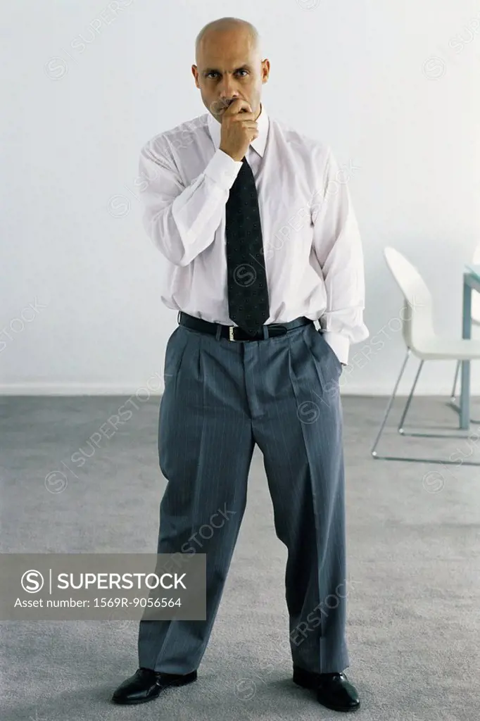 Business executive standing in office, looking thoughtfully at camera, full length portrait