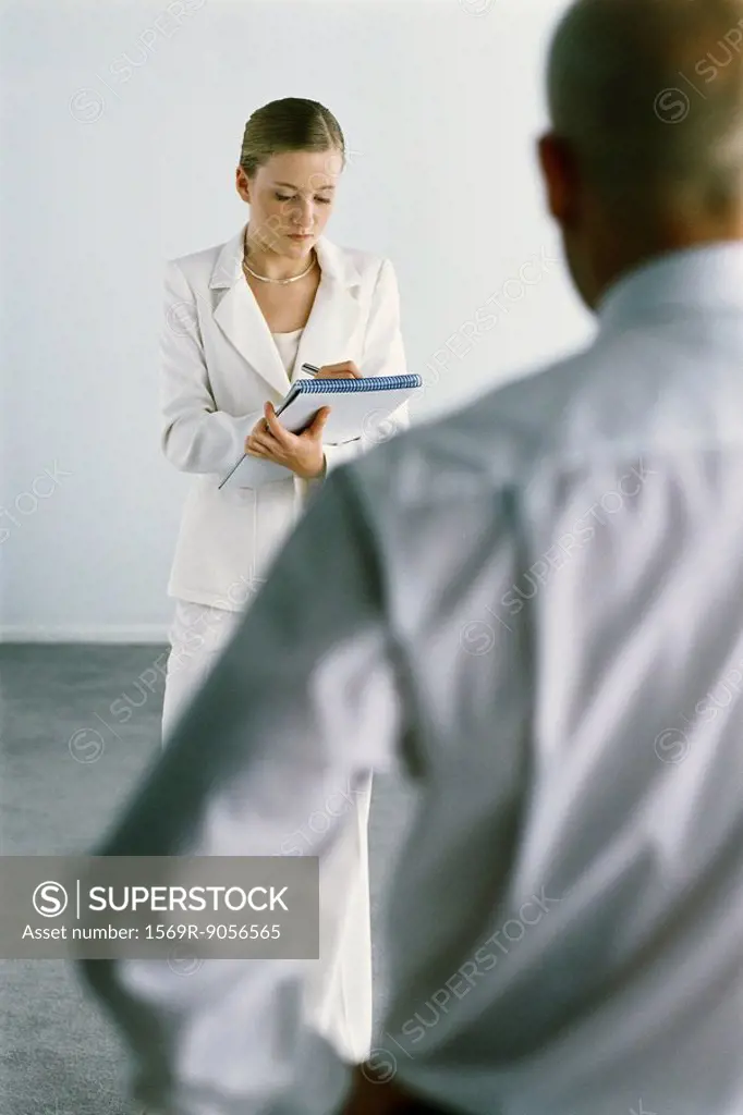 Young assistant standing taking notes, boss dictating in foreground