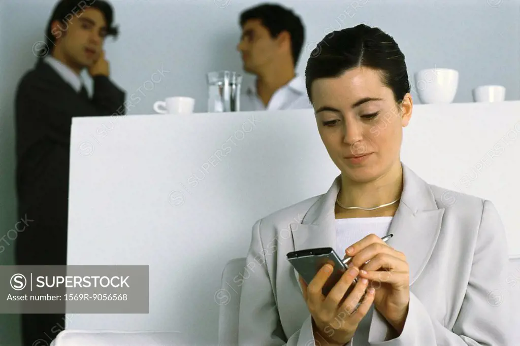 Young businesswoman using PDA while colleagues chat in background