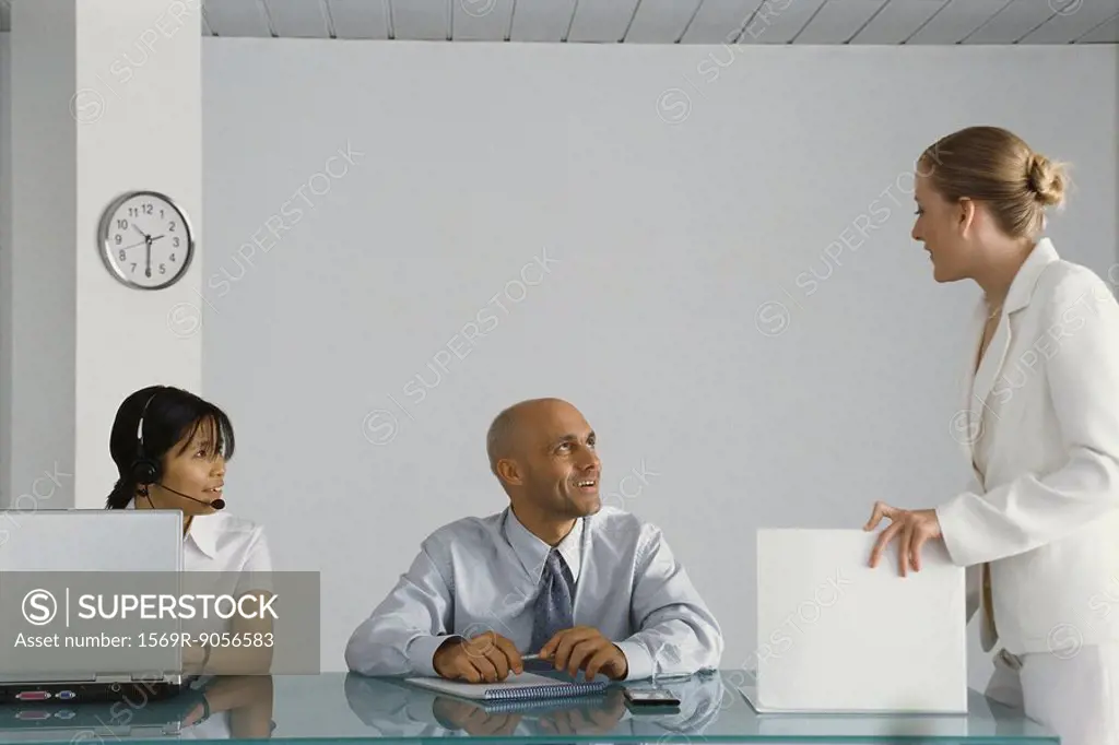 Young female executive standing by colleagues´ desk, conversing