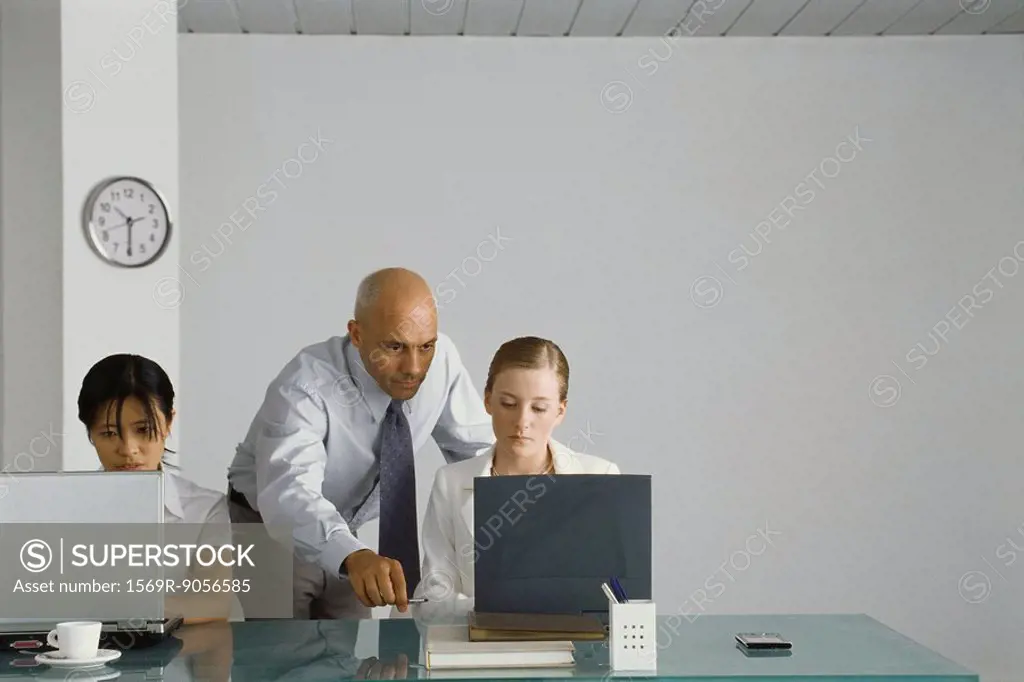 Professional man standing behind young female colleague, pointing at her computer screen