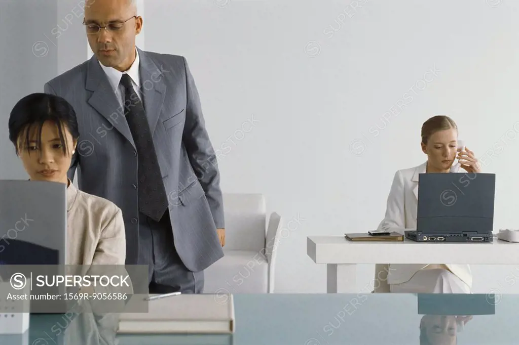 Manager standing, looking over shoulder of female employee while she works