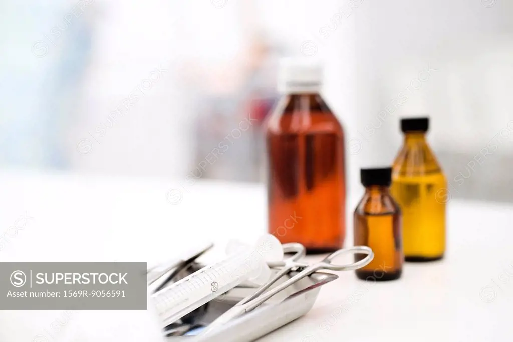 Medical tray with forceps, syringe, medicine bottles in background